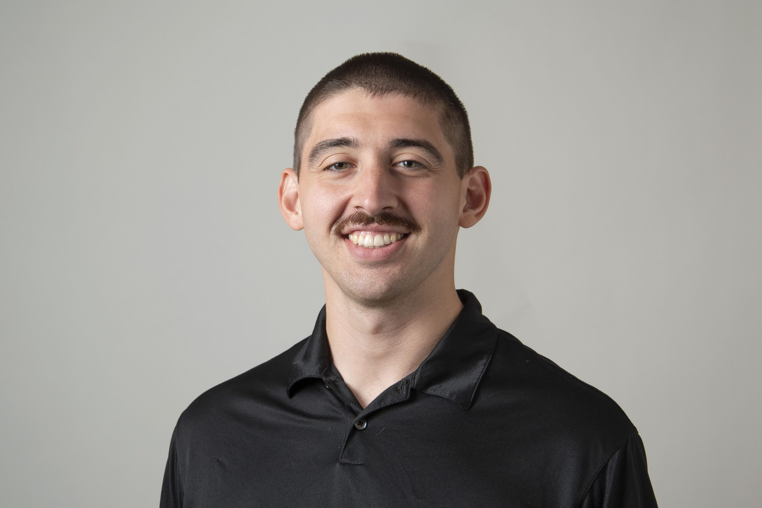 A man wearing a black polo shirt with a mustache